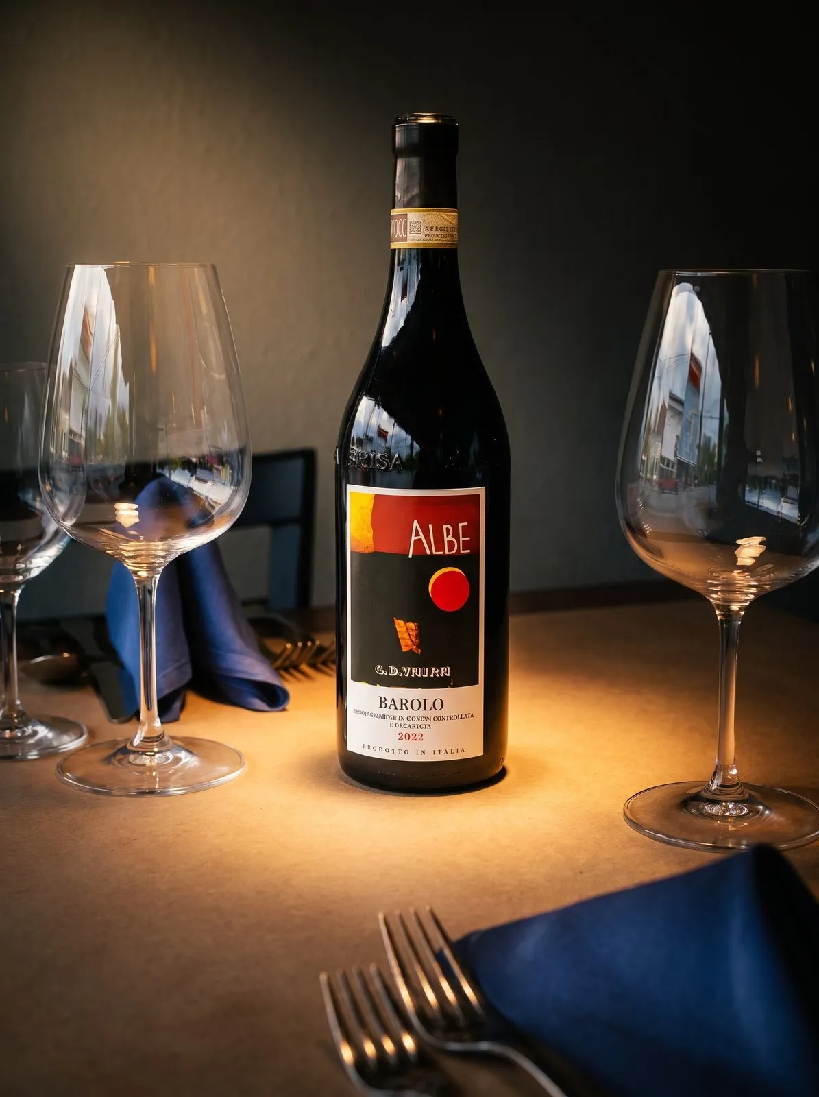 A bottle of Barolo Albe on a set table, warm light pooling around it.